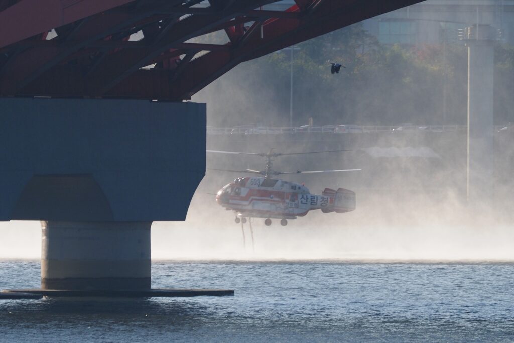 한강 서강대교 인근에서 하얀 물보라를 일으키며 호스 두 줄을 아래로 늘어뜨린 채 물을 채우는 산림청 헬기.