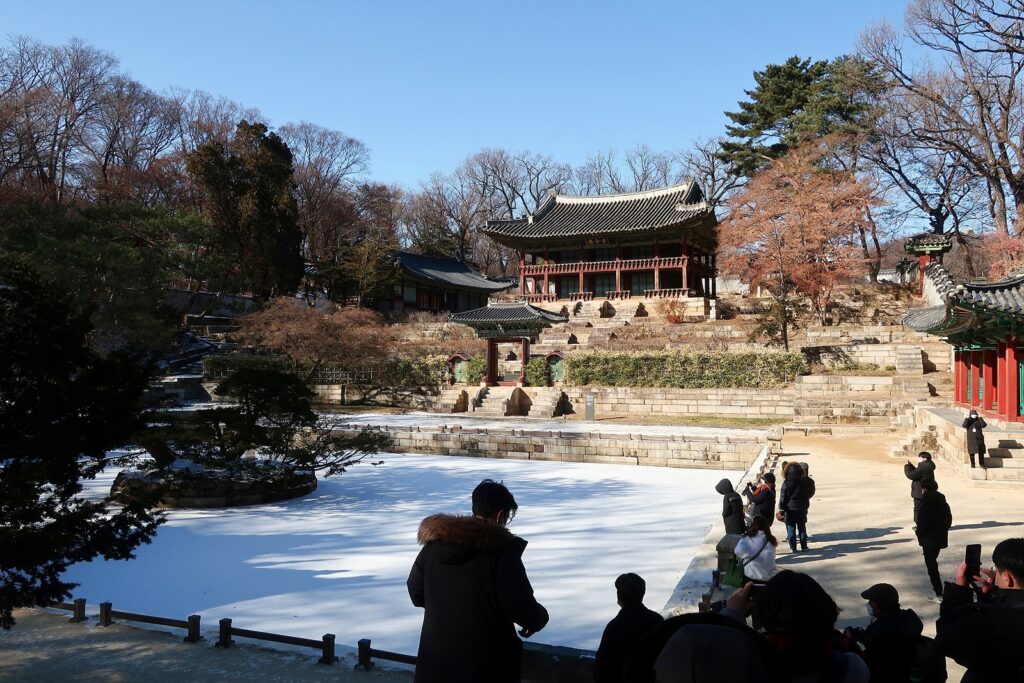 네모난 연못이 하얗게 얼어 있고, 주변에 관람객들이 있다. 연못 너머엔 주합루 건물이 서 있다.