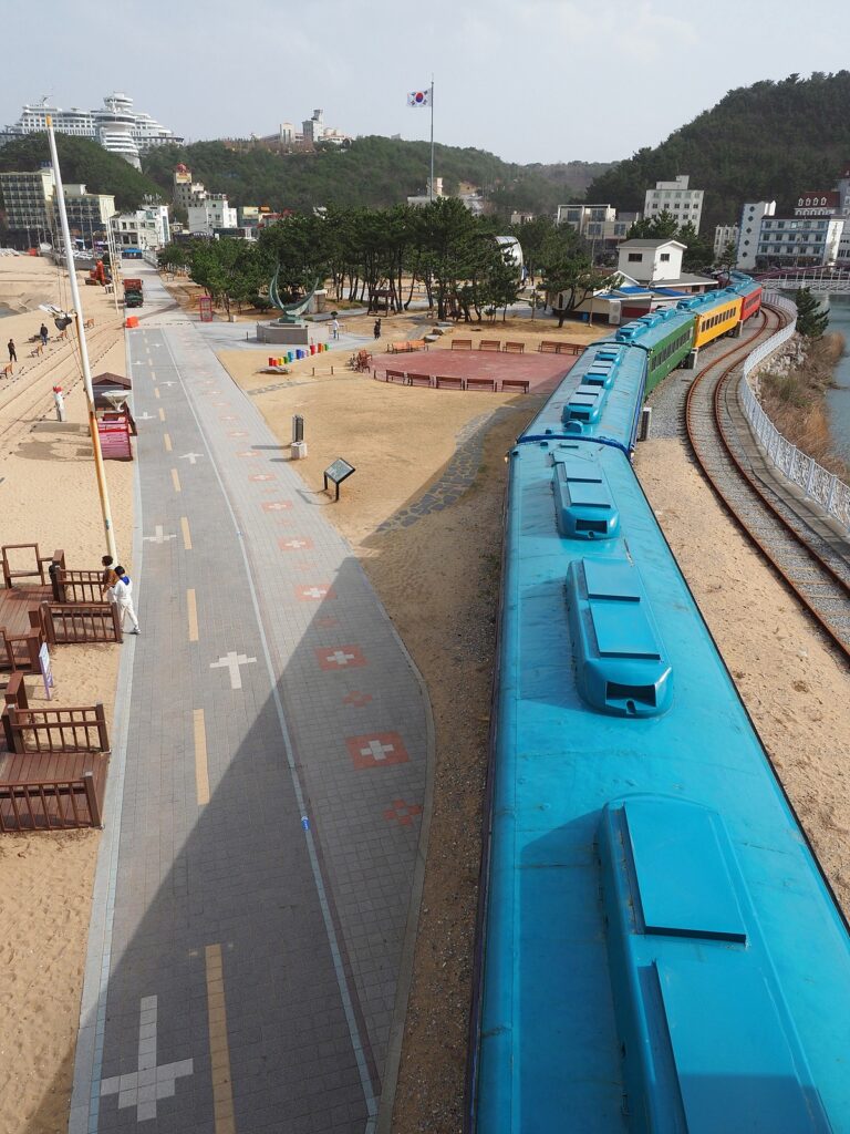 오른쪽으로 파란 지붕의 열차(시간박물관)와 철길이 누워 있고, 왼쪽으로는 인도가 지나간다. 그 옆으로 나무로 된 구조물이 몇 개 놓여 있다. 정면으로는 해시계와 침엽수 몇 그루가 있다.