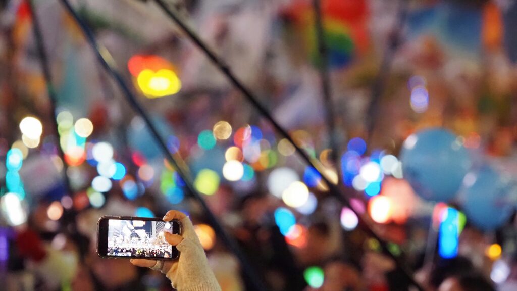 수많은 응원봉의 불빛이 빛나는 가운데, 한 시민이 휴대폰 카메라로 이를 촬영하고 있다.