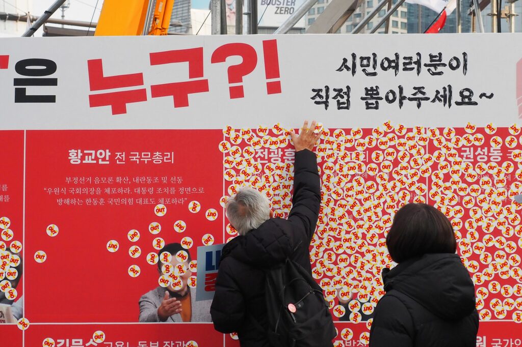"누구?!" "시민여러분이 직접 뽑아주세요~"라고 적힌 패널에 시민들이 스티커를 붙이고 있다.