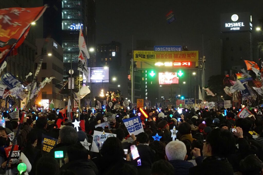 어두운 밤, 응원봉 불빛을 밝힌 시민들이 "윤석열 파면! 세종호텔 해고자 복직!"이라는 현수막이 걸려 있는 고공농성장 아래 모여 있다.
