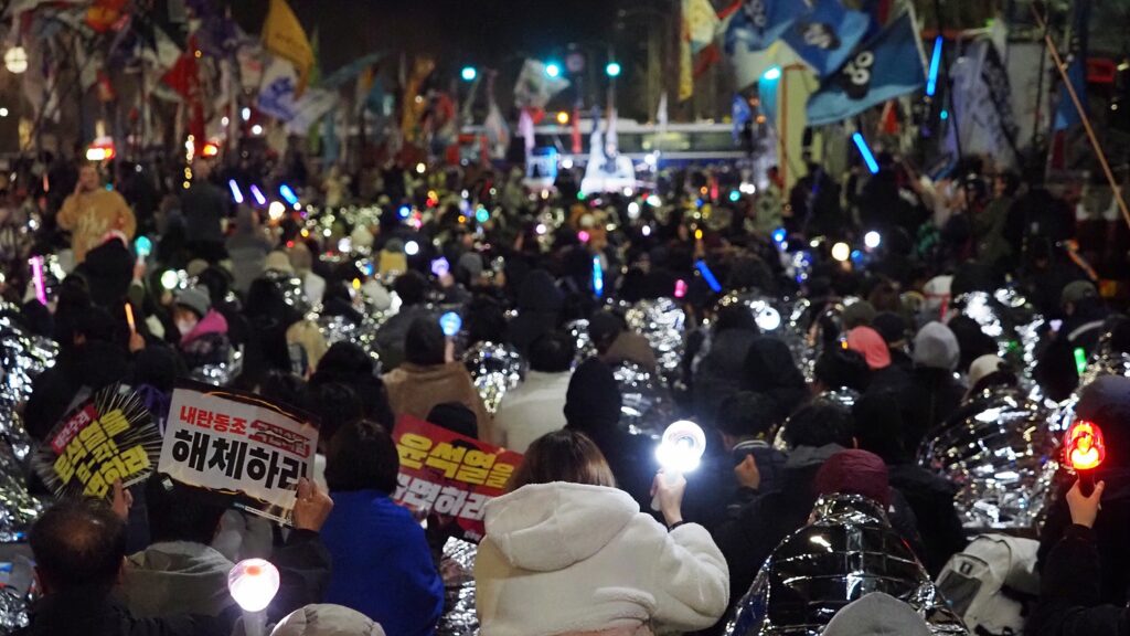 수많은 시민들이 "윤석열을 파면하라" 등의 손팻말과 응원봉을 들고 앉아 있는 모습.