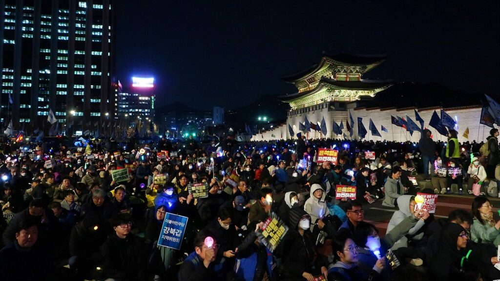 광화문 앞 야간 집회. 수많은 인파가 광화문 앞을 메운 채 빛나는 응원봉과 함께 "윤석열을 파면하라" 등의 문구가 적힌 팻말을 들어 보이고 있다.