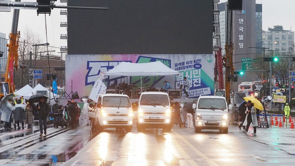 비에 젖은 도로에 비상행동 집회 관련 차량들이 서 있다. 시민들은 모두 돌아가고 광장이 텅 빈 상태다.